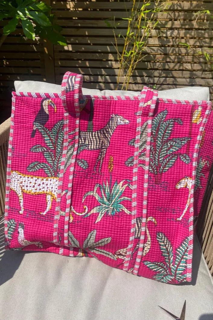 Pink tote bag with animal and plant patterns on a wooden surface